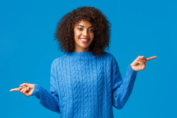 둘 다 괜찮아요 한 번보 세요. 겨울 스웨터를 입은 멋진 아프리카 계 미국인 아가씨는 손가락을 옆으로, 왼쪽 과 오른쪽을 가리키며 밝고 파란 배경을 미소짓는 두 가지 변종을 제안 한다. — 스톡 사진