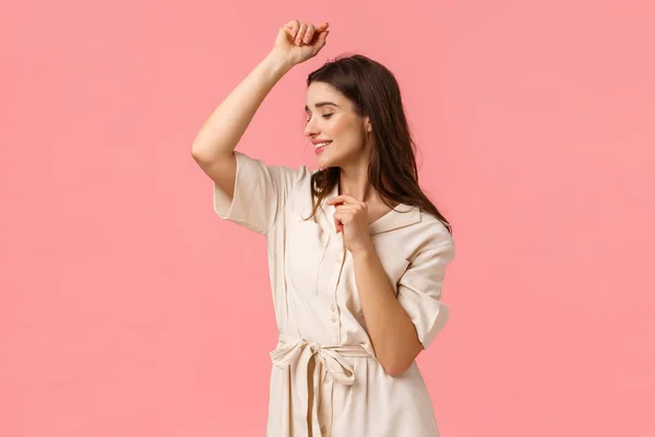 Romântico e sensual bela mulher em vestido, festa levantando as mãos para cima e sorrindo bonito, dançando desfrutando de lazer, se divertindo na viagem de fim de semana, de pé fundo rosa — Fotografia de Stock