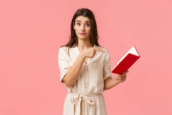 Did you wrote this. Intrigued brunette girl asking question about something written in notebook, pointing finger at note and looking puzzled, standing pink background confused — Stock Photo, Image