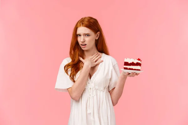 Girl dislike dessert, express aversion and disappoinment, touching neck as willing puke from awful tasty. Ignorant redhead female attend friends b-day party holding plate with cake, show disgust — Stock Photo, Image