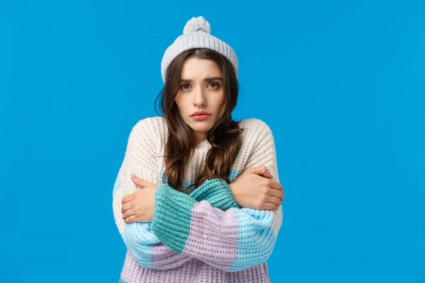 Άναψε το καλοριφέρ. Αναστατωμένη και μελαγχολική νεαρή ανόητη κοπέλα σε χειμερινό καπέλο, πουλόβερ, τρέμοντας από χαμηλή θερμοκρασία, αγκαλιάζοντας τον εαυτό της προθέρμανση, μίσος κρύα εποχή, μπλε φόντο — Φωτογραφία Αρχείου