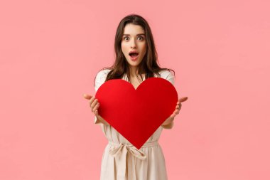 Sürprizler, hediyeler, ilişki konsepti. Çekici, çekici, çekici, çekici bir kız. Sevgi gösteren, kırmızı kalp kartını tutan, sevgililer gününü yaşatan, pembe arka planda duran.