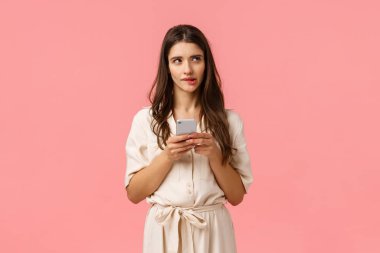 Meraklı ve rüya gibi bir kadın alışveriş meraklısı hangi sıranın en iyisi olduğunu düşünüyor, dudak ısırıyor görüntüye bakıyor, akıllı telefon tutuyor, riskli bir mesaj veriyor mu emin değilim, pembe arka planda duruyor düşünceli.