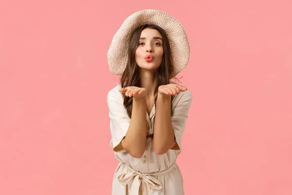 Conceito de ternura, glamour e romance. Mulher feminina elegante de boa aparência em chapéu e vestido, lábios dobráveis bobo soprando beijo de ar e enviá-lo com as palmas das mãos, dando amor, fundo rosa — Fotografia de Stock