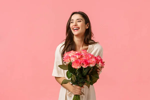 Día de San Valentín, romance, celebración y concepto de belleza. Encantadora mujer joven elegante y femenina recibe flores, sosteniendo hermoso ramo y riendo alegremente, fondo rosa — Foto de Stock