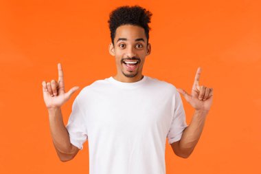 Heyecanlı ve ilgi çekici, şevkli Afro-Amerikan tişörtlü, bıyıklı afro saçlı, parmaklarını havaya kaldırmış, gülümseyen, mükemmel ürün gösteren, alışveriş merkezi, turuncu arka plan