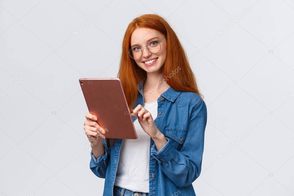 Waist-up portrait friendly happy redhead female student browsing online shops, holding digital tablet, picking new internet course for learning, smiling carefree looking camera, white background