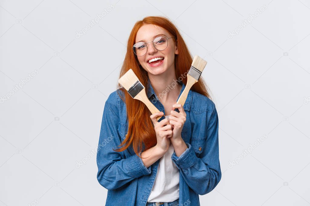 Waist-up portrait charismatic smiling, happy and creative redhead woman in glasses, laughing joyfully showing paintbrushes and grinning, creating new artwork, paint walls, help friend with repair