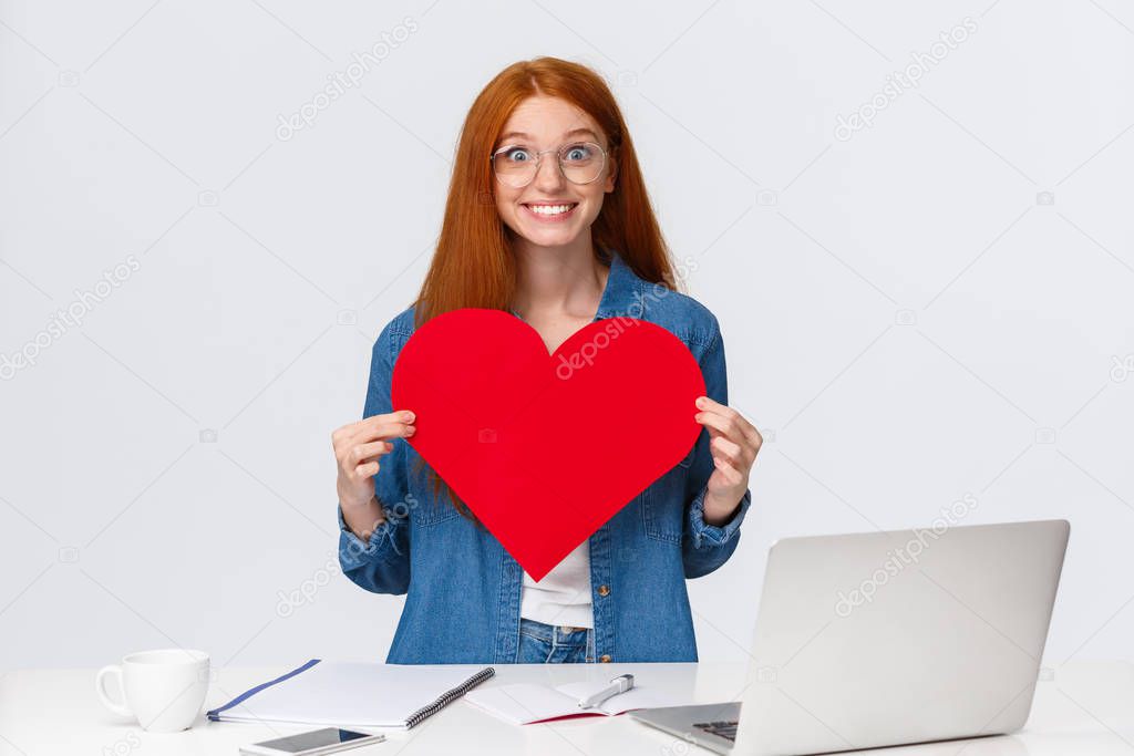 Cheerful and excited cute girlfriend with red hair, cant wait give big red valentines heart to boyfriend, showing sympathy, confess in love, celebrating lovers day, standing white background