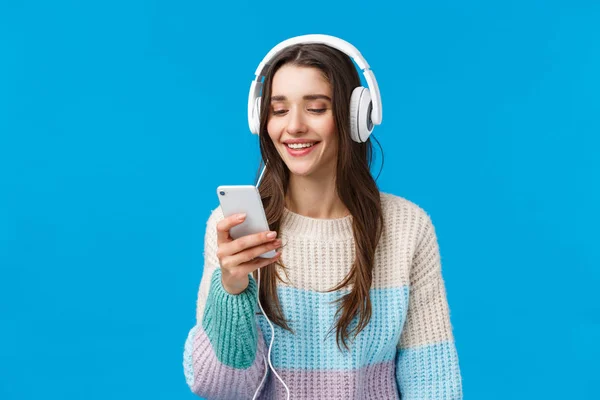 Technologie, milléniaux et concept de style de vie. Insouciante étudiante brune mignonne mettre des écouteurs, plug-in smartphone cueillette chanson et sourire, debout fond bleu faire une playlist pour l'étude — Photo