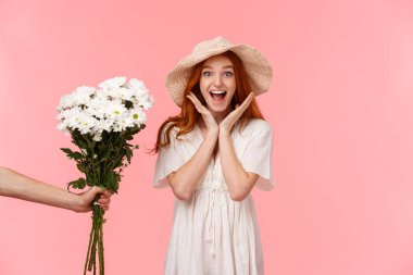 Sürprizler, kutlamalar ve tatil konsepti. Şaşırmış mutlu ve neşeli gülümseyen kızıl saçlı kız mutluluk ve neşe çığlıkları atıyor, ona çiçek veren biri gibi, pembe arka plan