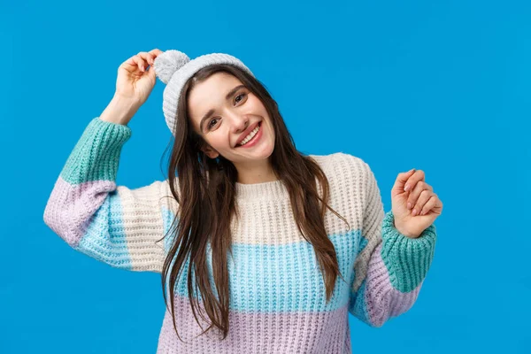 Vrij vrolijke en vrolijke, lachende jonge vrouw vieren kerst, wintervakantie, dansen en plezier hebben op skigebied, bergen, het dragen van hoed en trui, staan gelukkig over blauwe achtergrond — Stockfoto