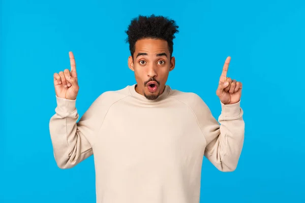 Have you seen it. Attractive impressed african-american guy with moustache, afro haircut, saying wow, telling about event, product advertising, pointing fingers up over blue background — Stock Photo, Image