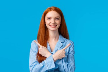 Neşeli kız reklamları iki ürün, yol ya da seçenek sunuyor, çapraz ellerle sağa sola işaret ediyor, gülümsüyor, keyif alıyor, pijama giyiyor, mavi arka planda duruyor.