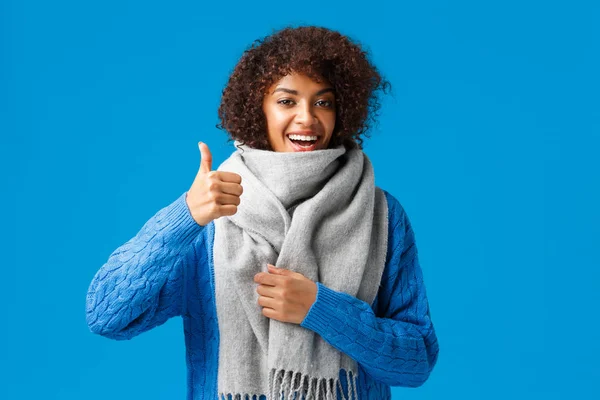 Very good, yes. Cute happy african-american woman in sweater, bought cool warm and comfortable scarf showing thumb-up in approval, recommend shop, standing blue background — 스톡 사진