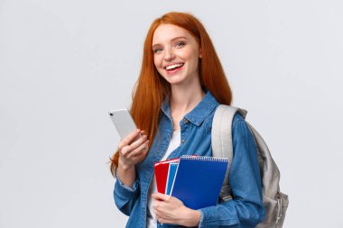 Karizmatik, mutlu, gülümseyen kızıl saçlı genç kız sırt çantalı, defterli üniversite öğrencisi, elinde akıllı telefon, mesajlaşan arkadaş, sohbet ya da taksi çağıran, sırıtan asansör kamerasını bekleyen.