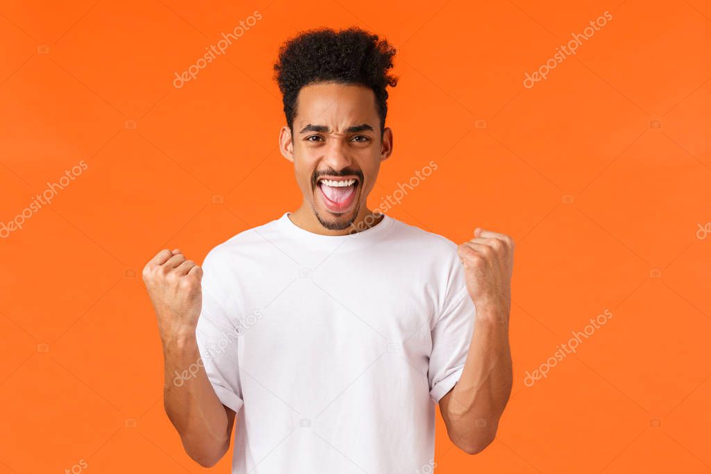 Yes I did it. Winner and champion, relieved satisfied african-american guy feeling confident, flex biceps, fist pump and saying yeah triumphing, achieve success or prize, win bet, orange background