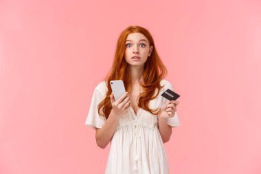 Dikkati dağılmış, tatlı kızıl saçlı kız kameraya cevap vermek için başını kaldırdı. Kameraya baktı, elinde akıllı telefon ve kredi kartı vardı. İnternetten satın almak için para ödemeye çalıştı.