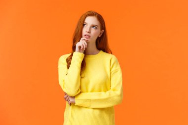 Ciddi ve kararlı genç ve zeki kızıl kız hesaplamalar yapıyor, çeneye dokunuyor düşüncelere odaklanmış bir yüz ifadesiyle düşünüyor, seçim yapıyor, çözüm arıyor ya da bulmacayı çözüyor, düşünceli duruyor.