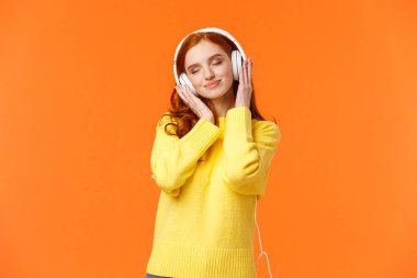 Kulaklığın yumuşak sesinden hoşlanan bir kız. Neşeli romantik ve neşeli kızıl saçlı güzel bir kadın. Gözleri kapalı, tatlı bir gülümsemesi var. Kulaklıkla müzik dinliyor.