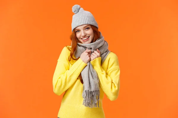 Robi się zimno na zewnątrz. Cute i piękne rudowłosa kobieta nosić szary zimowy kapelusz i szalik, coraz ciepłe przygotowanie grać śnieżki z przyjaciółmi na zewnątrz podczas ferii zimowych, pomarańczowe tło — Zdjęcie stockowe
