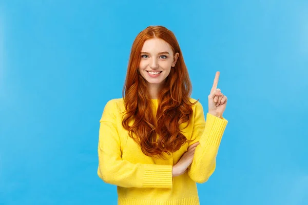 Aantrekkelijk zelfverzekerde en charismatische blanke roodharige vrouw in gele trui, toon nummer een, product bestellen, wordt als eerste, glimlachend tevreden en assertief, staande blauwe achtergrond — Stockfoto