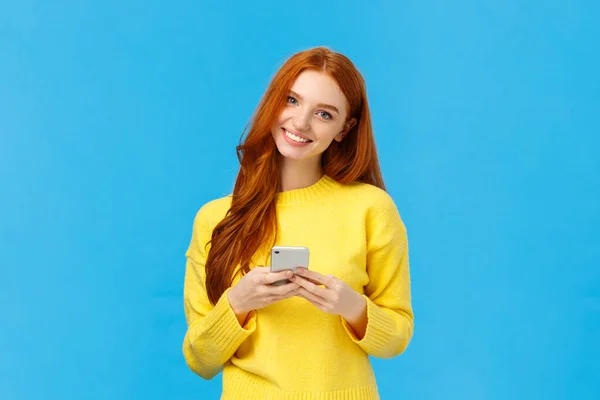 Technology, internet and gadgets concept. Cute redhead woman sending text friend, messaging, having conversation using smartphone app, smiling camera, download useful application, blue background — Stock Photo, Image