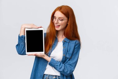 Teknoloji ve insan konsepti. Üniversite için tasarım projesi hazırlayan çekici, yaratıcı, genç bir kızıl kız elinde dijital tablet, beyaz arka planda, cihaz ekranında bir şey sunuyor.