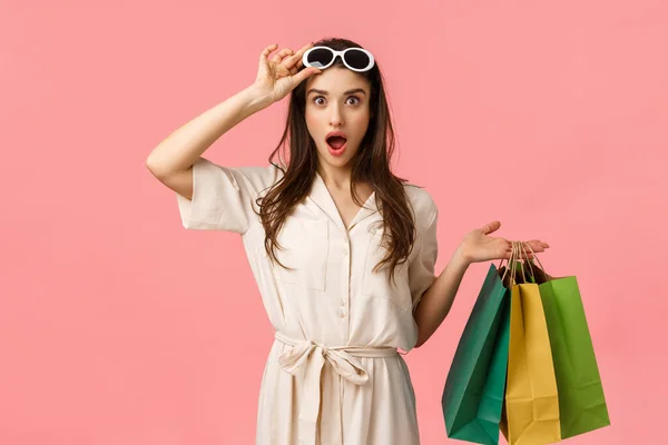 Lasst uns einkaufen gehen. Amüsierte und aufgeregte Shoppaholic-Frauen, die Spaß daran haben, durch Einkaufszentren zu stöbern, Einkaufstaschen in der Hand zu halten, die Brille auszuziehen und genau zu sehen, was sie suchen, rosa Hintergrund — Stockfoto