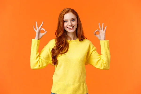 Concepto de idea perfecta, aceptación. Chica pelirroja guapa en suéter amarillo, mostrando bien, buena o aprobación signo sonriente asentir acuerdo, satisfecho con el resultado, todo perfecto, fondo naranja — Foto de Stock