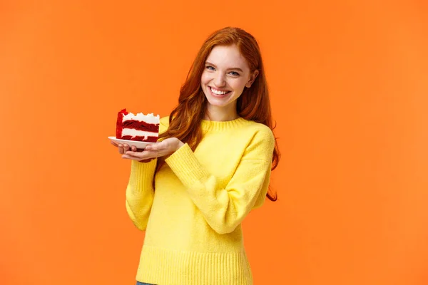 Cute friendly redhead woman holding tasty home-made piece cake and smiling, share bite, treat friends, grinning as celebrating birthday or like eating sweet delicious desserts, orange background — Stock Photo, Image