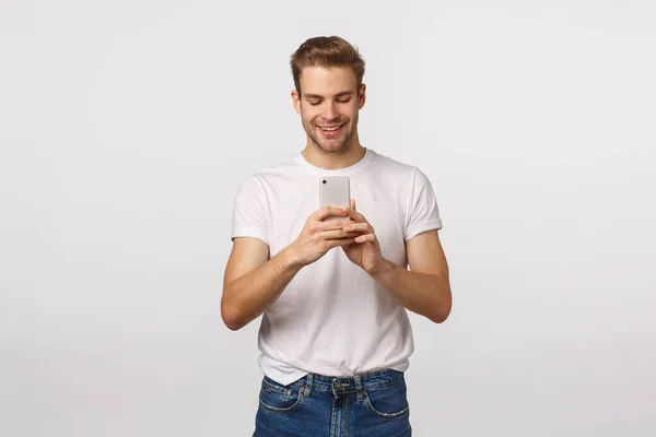 Entusiastiska snygg och söt blond pojkvän ta foto för flickvän, skytte händelse, spela in video på smartphone, hålla mobiltelefon och titta på skärmen med glada leende, vit bakgrund — Stockfoto