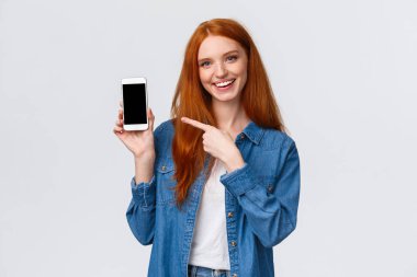 Belden yukarı portre neşeli karizmatik kadın eleştirisi akıllı telefon uygulaması. Fotoğrafını sevimli filtreyle gösteriyor. Cep telefonu ekranını ve gülümseyen kamerayı işaret ediyor.