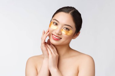 Asyalı güzel bir genç kadın, gözlerinin altında altın maskelerle cildini önemser.