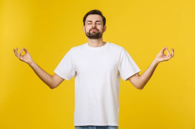 Beyaz beyaz erkek tişörtü gri stüdyo arka planında tek başına duruyor, parmaklarını katlıyor stresi azaltmak için nefes egzersizleri yapıyor.