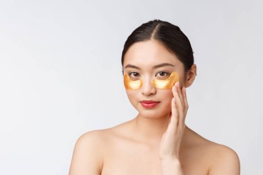 Asyalı güzel bir genç kadın, gözlerinin altında altın maskelerle cildini önemser.