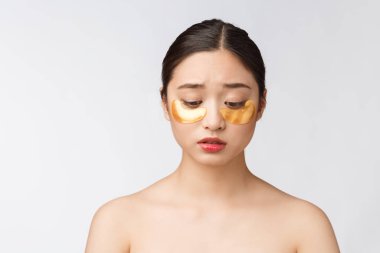 Asyalı güzel bir genç kadın, derisini altın göz maskeleriyle, göz altı bantlarıyla kaygıyla önemser..