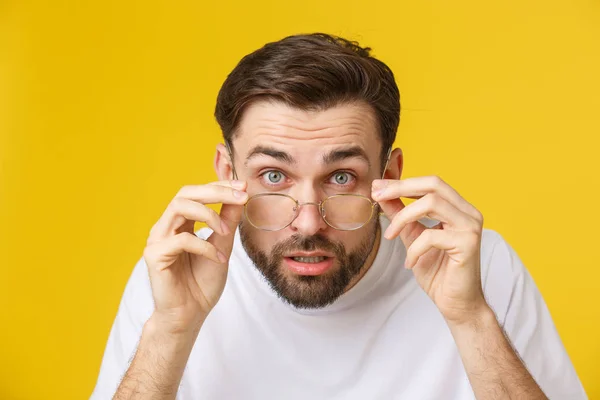 Närbild av ung stilig man ser och visar roligt ansikte vid kameran, bär glas. Isolerad vy på gul bakgrund. — Stockfoto