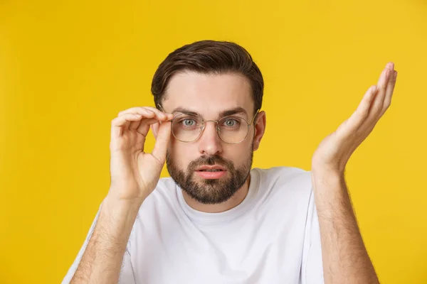 Fechar-se de homem bonito jovem olhando e mostrando cara engraçada na câmera, vestindo vidro. Vista isolada sobre fundo amarelo . — Fotografia de Stock