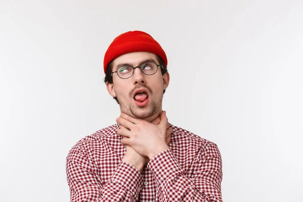 Close-up retrato de cara barbudo engraçado sufocando-se língua vara como se não pode respirar, rolar os olhos fingir morrer de tédio ou expressar sua angústia, de pé em gorro vermelho e óculos — Fotografia de Stock