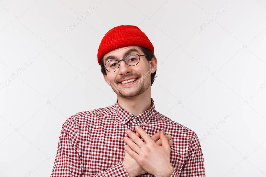 Close-up portrait funny and cute bearded caucasian hipster guy in red beanie and checked shirt, wear glasses, smiling thankful, receive confession or praises, touch heart grateful