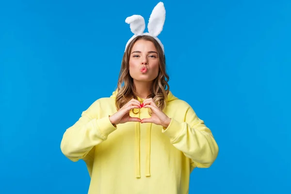 Vacances, traditions et concept de célébration. Funny et mignonne fille blonde idiote en sweat à capuche jaune et oreilles de lapin montrant geste de coeur, faire mwah embrasser expression, répandre l'amour et la positivité — Photo