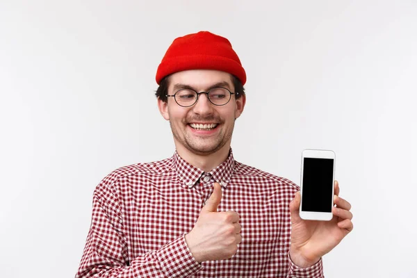 Teknik och människor koncept. Närbild porträtt nördig söt skäggig man med glada glada leende, tittar på mobiltelefon display ge tummen upp i approvel, föreslå cool app, vit bakgrund — Stockfoto