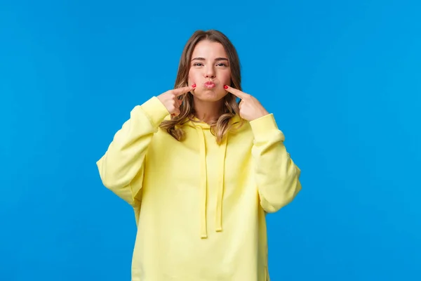 Concepto de mujeres, estilo de vida y emociones. Retrato de chica tonta y despreocupada tonteando, conteniendo la respiración y haciendo pucheros, metiendo mejillas tratando de no reír, mostrando una sonrisa linda, mira cámara, fondo azul —  Fotos de Stock