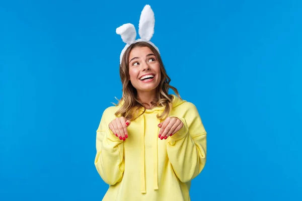 Vacances, traditions et concept de célébration. Rêve et mignon jeune femme souriant belle avec des oreilles de lapin, regarder optimiste coin supérieur droit sourire faire geste pattes, fond bleu — Photo