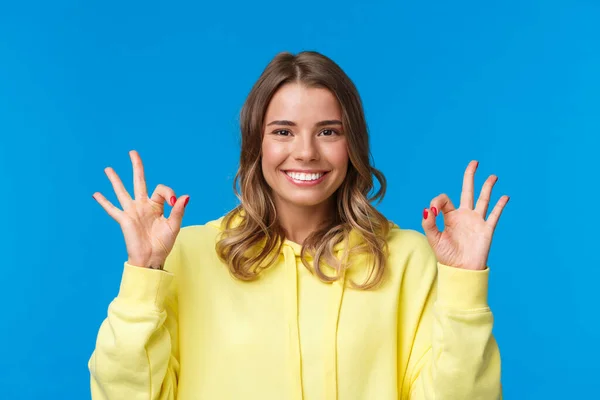 Close-up portrait happy confident young blond girl assure all okay, guarantee plan went well, smiling and show ok gesture in approval, confirmation or like, stand blue background — 图库照片