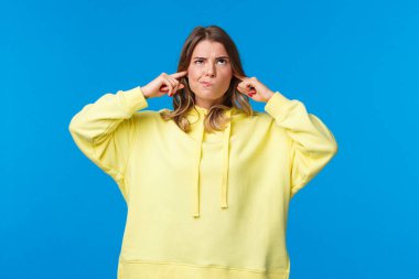 Disturbed and bothered young blong woman with pissed-off expression, grimacing boiling from annoyance and anger at her loud neighbours, shut ears cursing in mind look up
