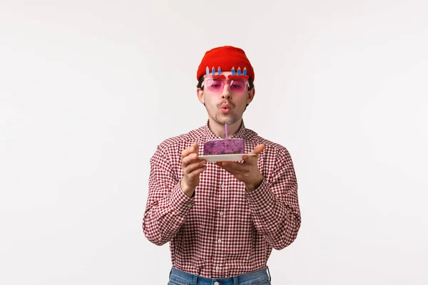 Celebration, holidays and lifestyle concept. Cute adult caucasian man celebrating his birthday in funny sunglasses, friends throw party, sing song as he blow out candle on b-day cake — Stock Photo, Image