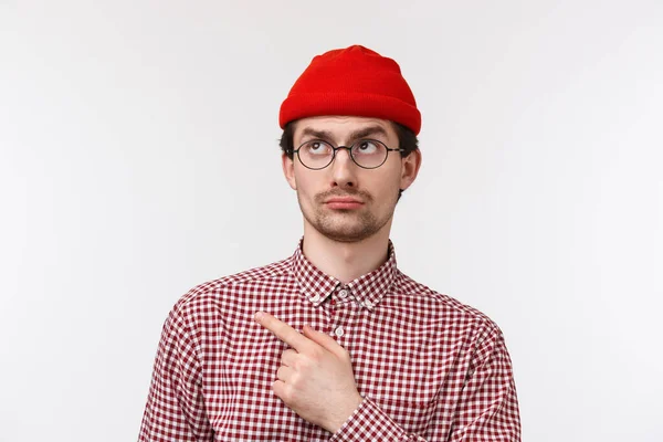 Skeptical and unimpressed handsome young hipster guy look judgemental and displeased, pointing staring upper left corner disappointed, standing white background reluctant — Stockfoto