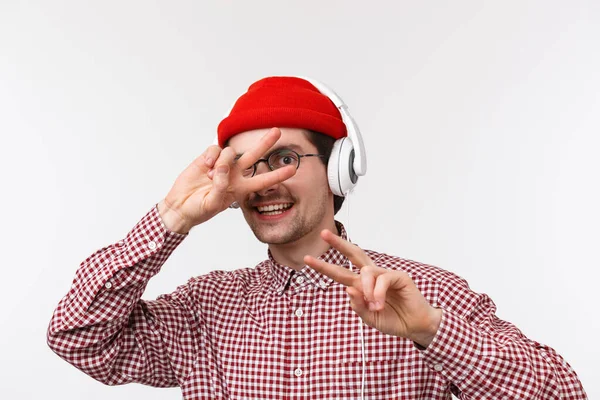 Muzyka, technologia i koncepcja ludzi. Close-up portret szczęśliwy młody człowiek z wąsami i brodą, nosić hipster czerwony kapelusz, słuchanie muzyki w słuchawkach i pokazać znaki pokoju — Zdjęcie stockowe